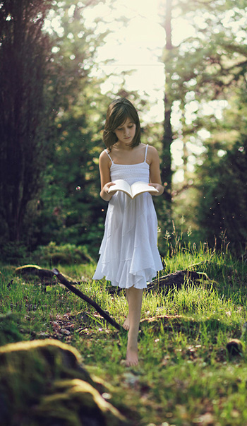 Fotografía creativa niña leyendo por el bosque